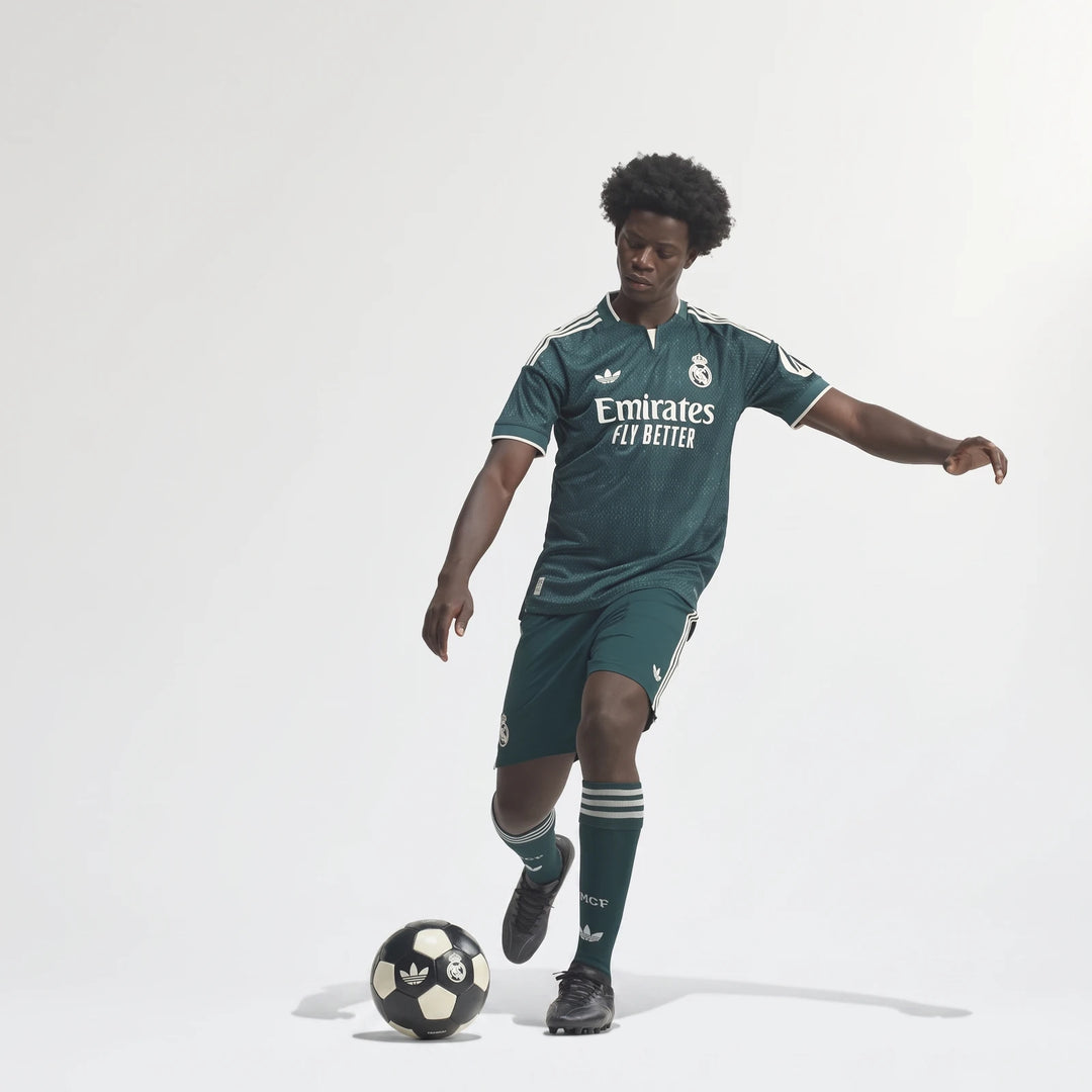 Male model wearing Real Madrid 26/27 Away Authentic Jersey in green with white details, playing soccer with a ball.