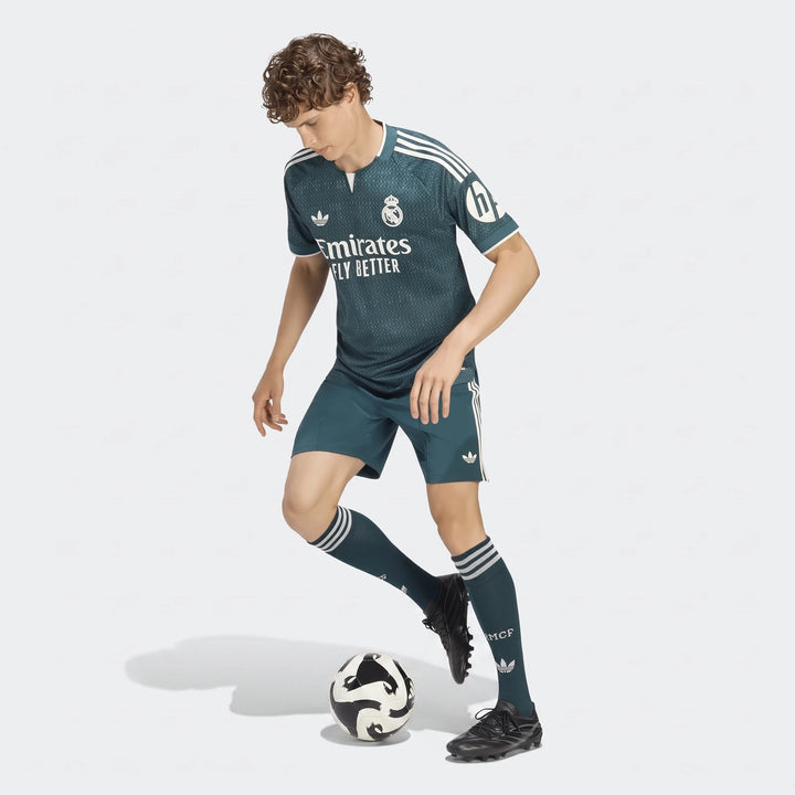 Real Madrid 26/27 Away Authentic Jersey on a male model in a teal soccer kit with white details, dribbling a soccer ball.