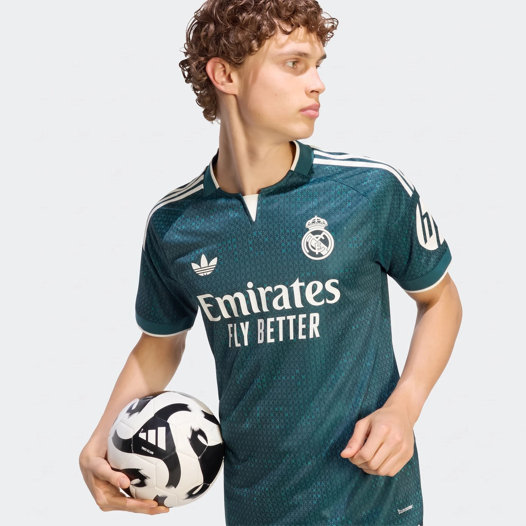 Male model wearing a dark green Real Madrid 26/27 Away Authentic Jersey and holding a black and white soccer ball in a