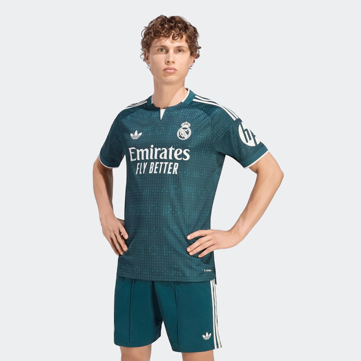 Male model wearing Real Madrid 26/27 Away Authentic Jersey in teal with matching shorts, shown front-on with hands on hips.