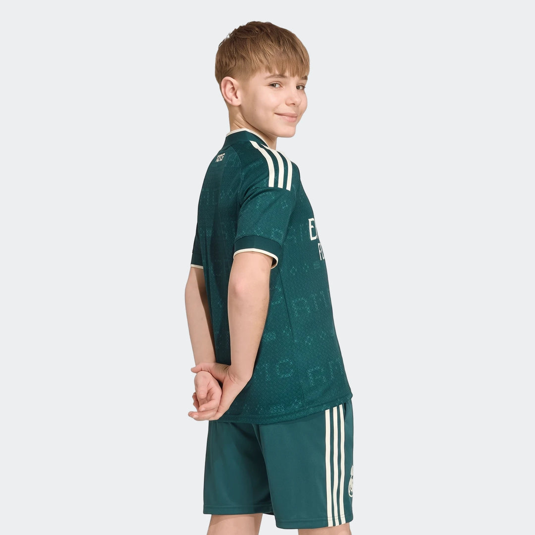 Young boy wearing a dark green Real Madrid 26/27 Away Jersey with matching shorts, featuring white three stripes.