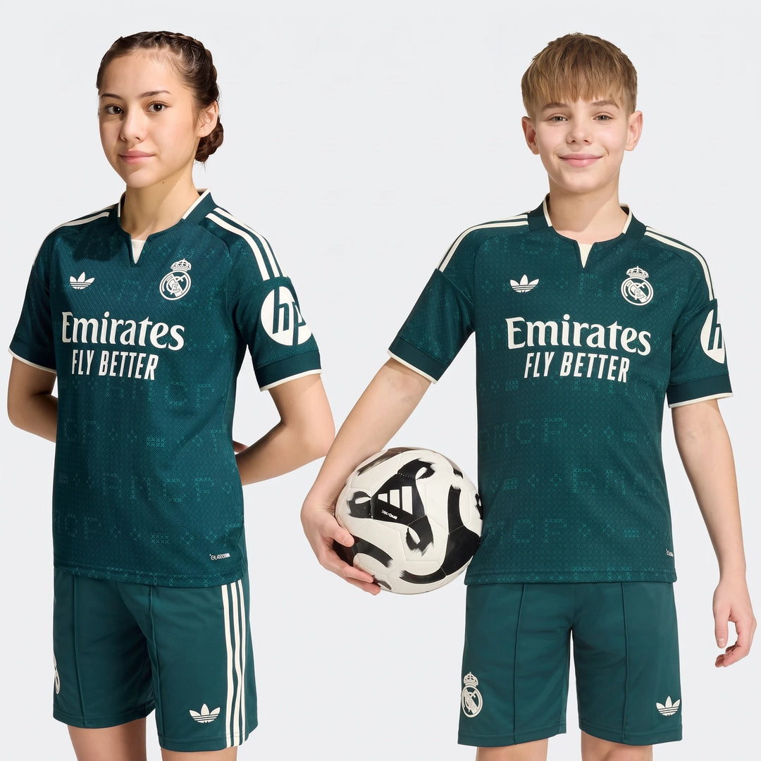 Two young models wearing green Real Madrid 26/27 Away Kids jerseys and shorts, standing on a white background.