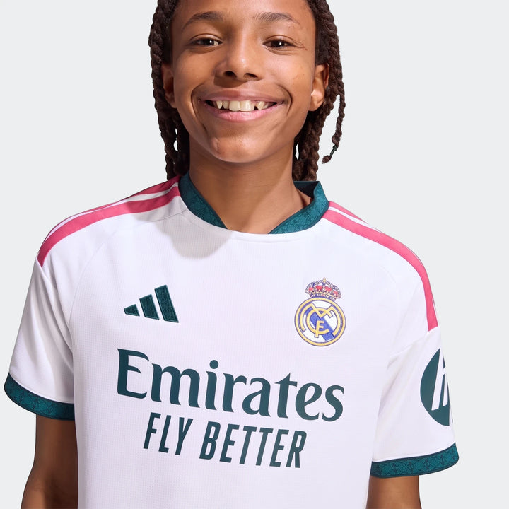 Close-up of a smiling kid wearing a white Real Madrid 26/27 Home Jersey with pink and teal details.
