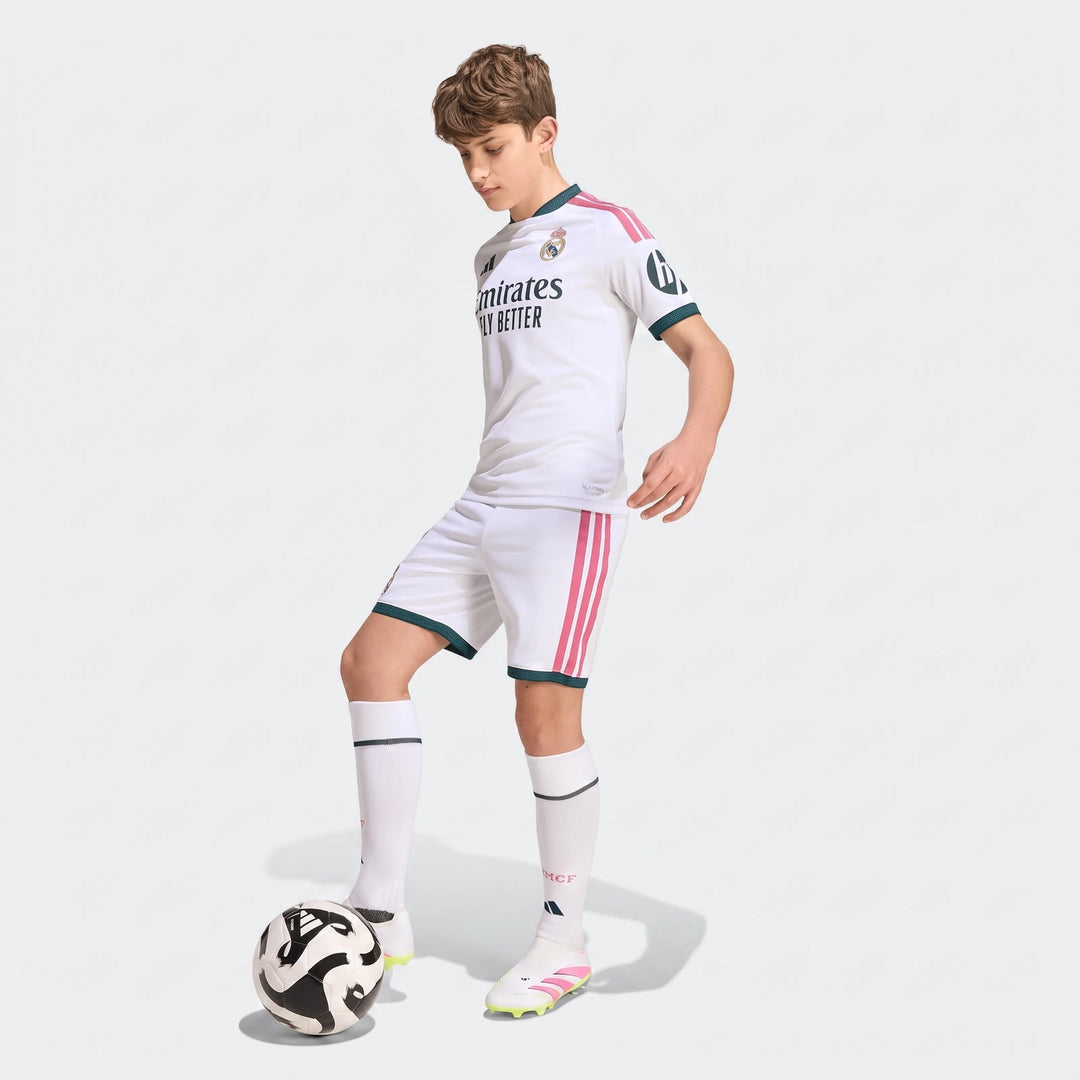 Young male model wearing white Real Madrid 26/27 Home Kit, including jersey and shorts, with a soccer ball. Football uniform