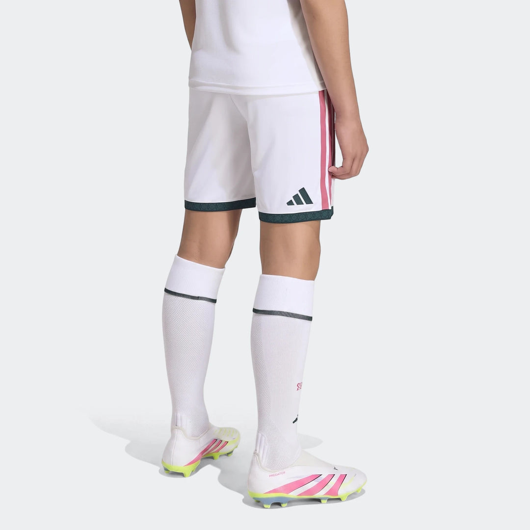 Real Madrid 26/27 Home Shorts Kids in white with pink stripes, dark green Adidas logo, worn by a child from a back view,