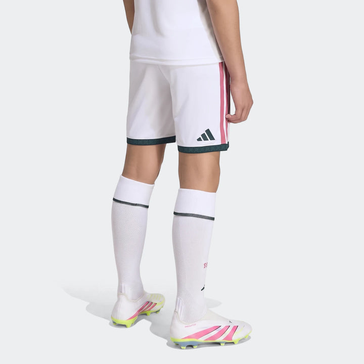 Real Madrid 26/27 Home Shorts Kids in white with pink stripes, dark green Adidas logo, worn by a child from a back view,