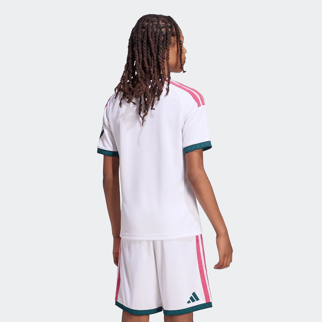 Back view of a youth wearing the white Adidas Real Madrid 26/27 Kids Home Jersey and matching shorts with pink stripes.