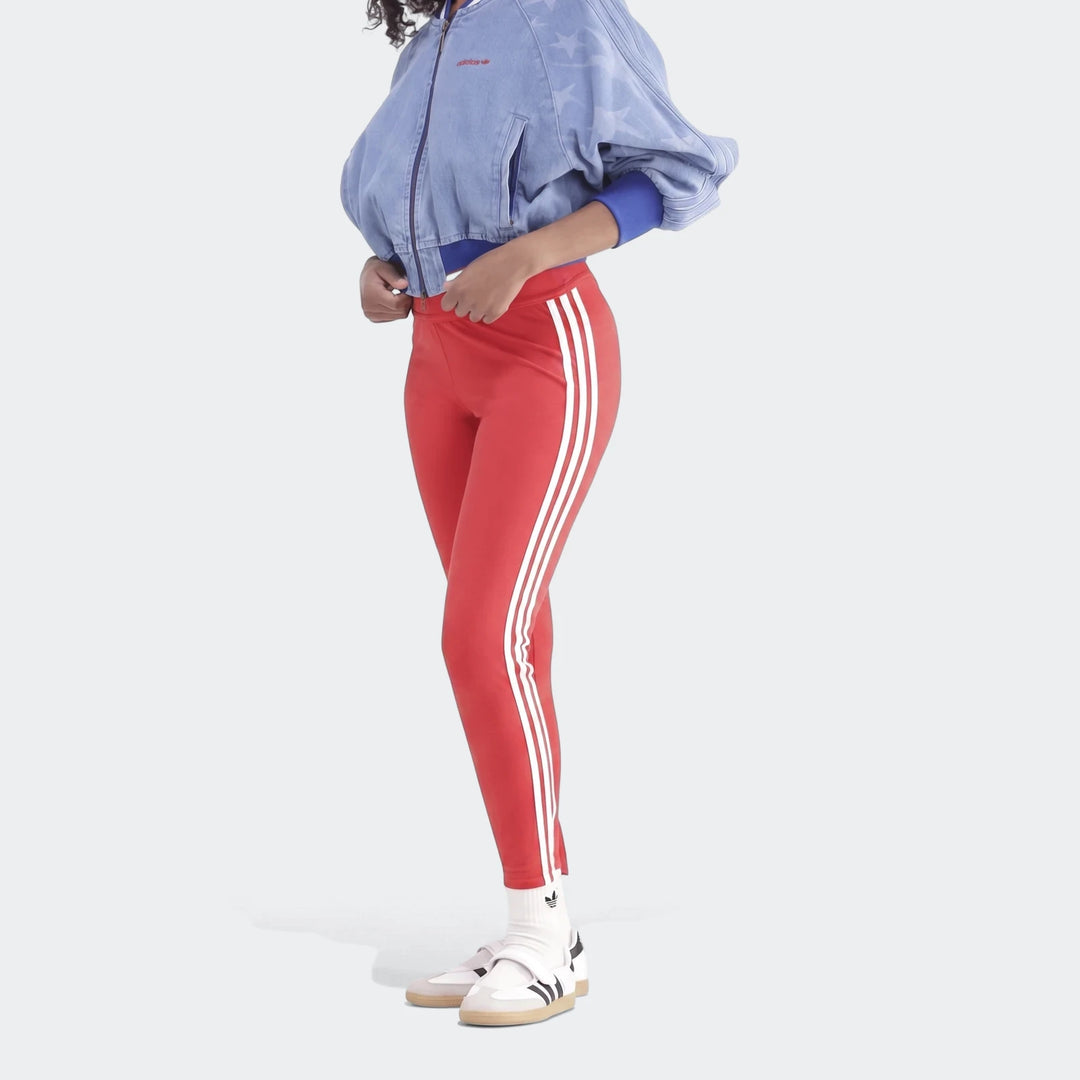 Model wearing red Adidas 3-Stripes Cotton Leggings with white stripes and a blue denim jacket on a gray background.
