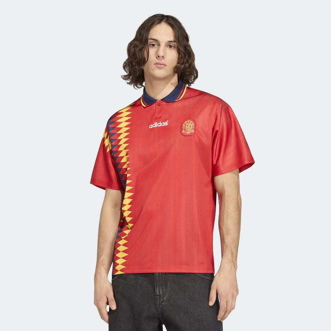 Male model wearing a red Adidas Spain national football team jersey with a polo collar and patterned side panel, front view.