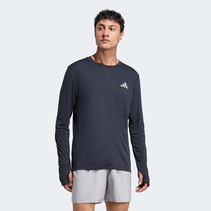 Male model wearing a dark grey Run Essentials Long Sleeve Top with thumbholes and light grey shorts, presented in a front