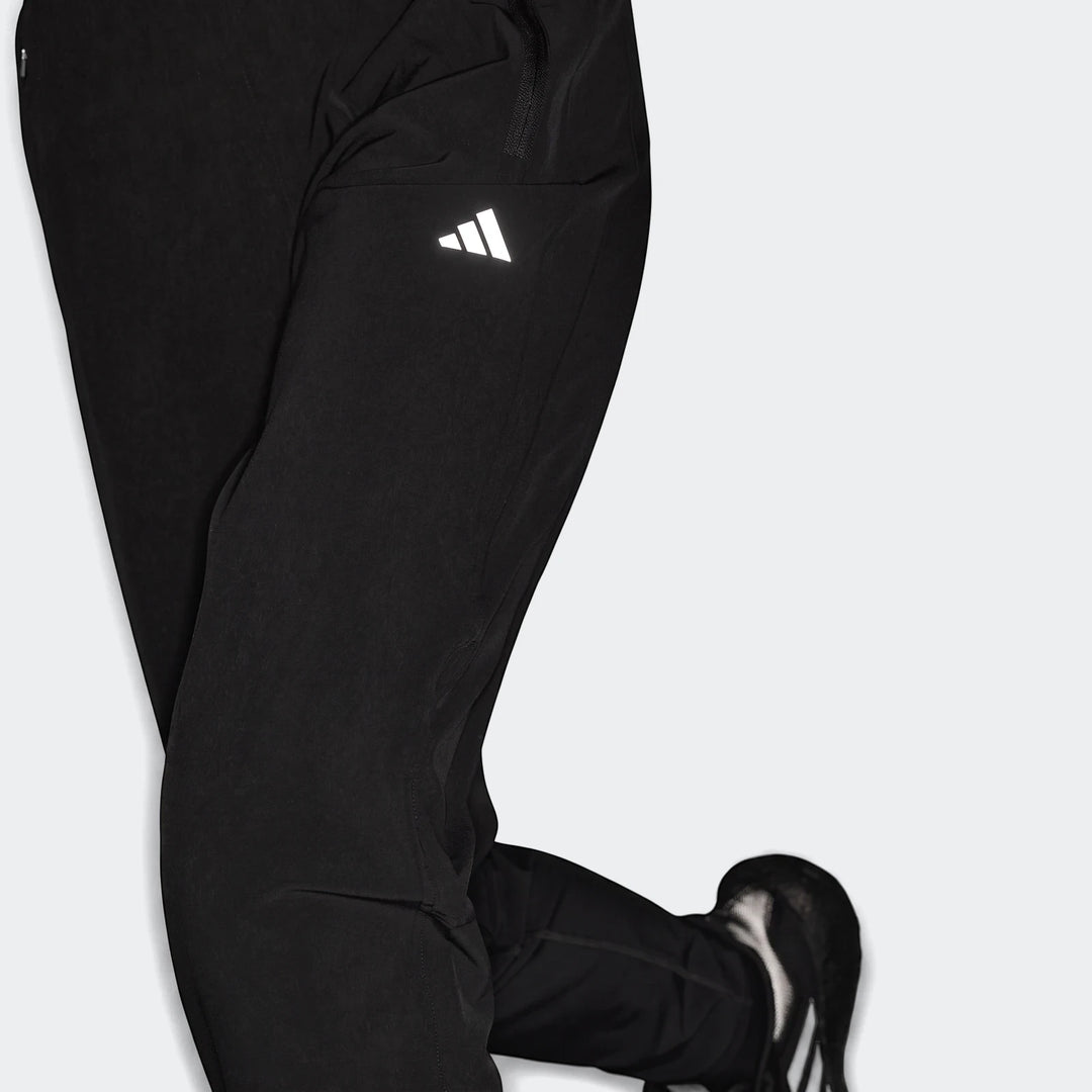 Black Adidas Run It Tko Joggers on a person, featuring a reflective white logo and zipper detail, with part of an athletic