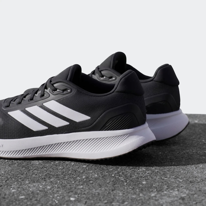 Angled view of black Adidas Runfalcon 5 sneakers with white three stripes and white soles, showcasing their design.