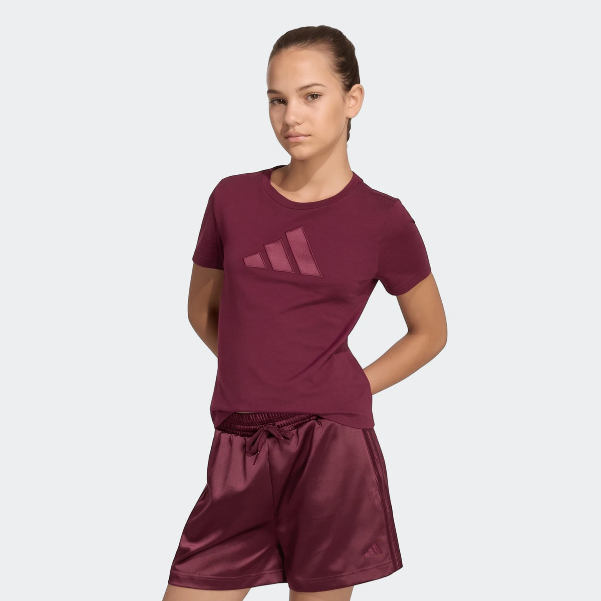 Model wearing a burgundy satin T-shirt with a subtle stitched logo on the chest.