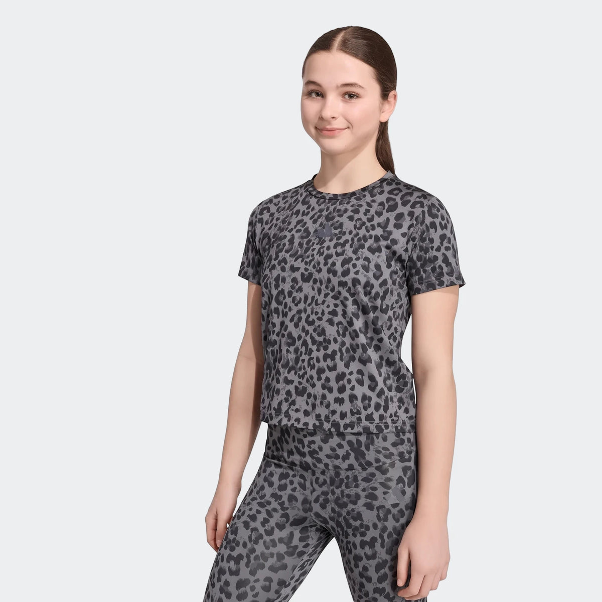 Young woman in a grey leopard print short-sleeve sport t-shirt and matching leggings, standing.