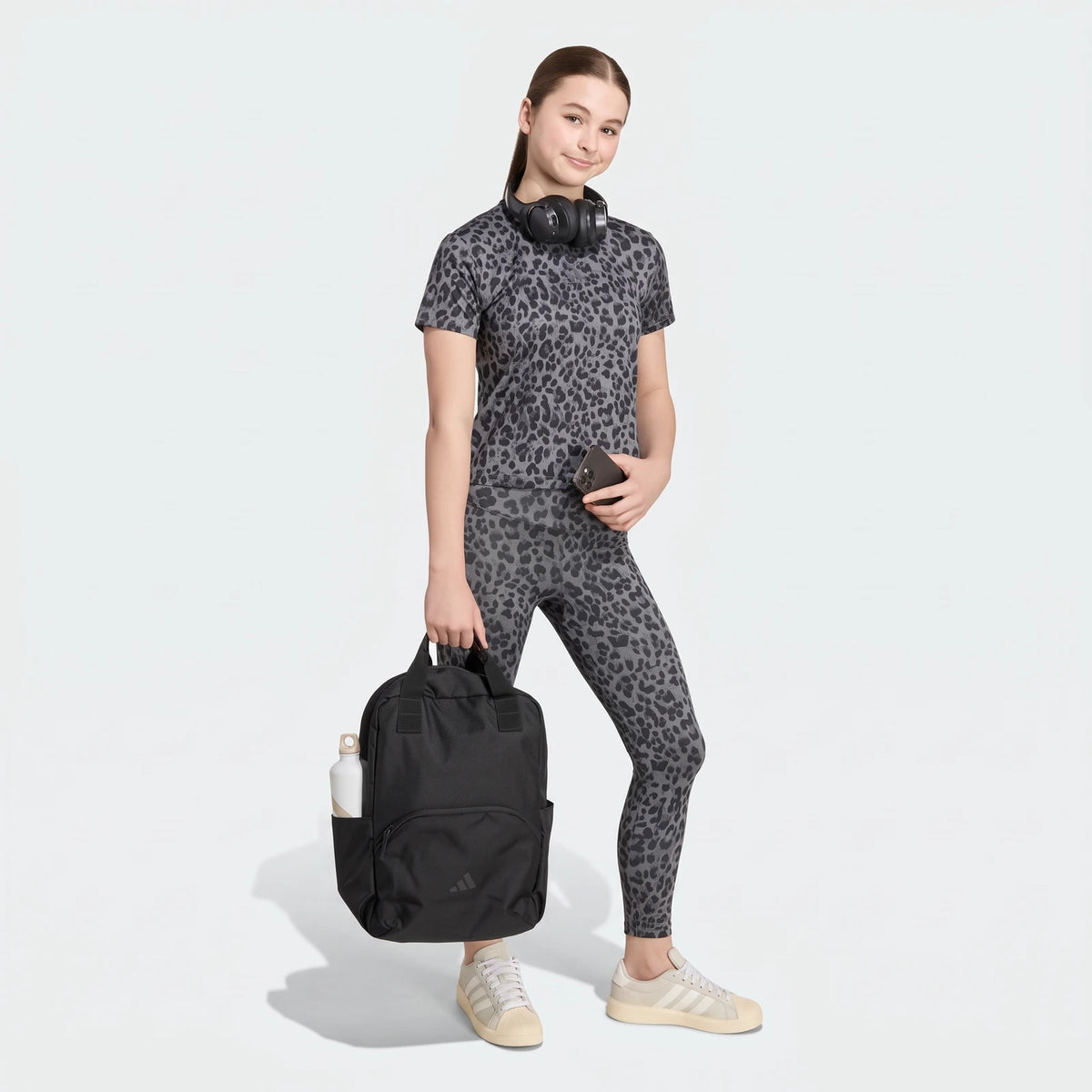 Young woman in a gray leopard print Seasonal Animal Print Sport T-Shirt and matching leggings, carrying a black backpack and
