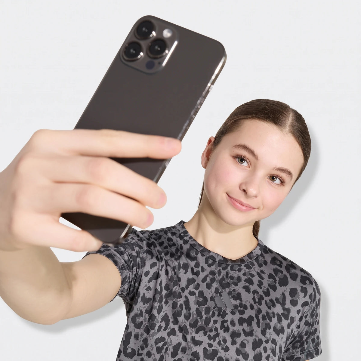 Young woman in a grey leopard print short sleeve sport t-shirt taking a selfie with a dark smartphone.