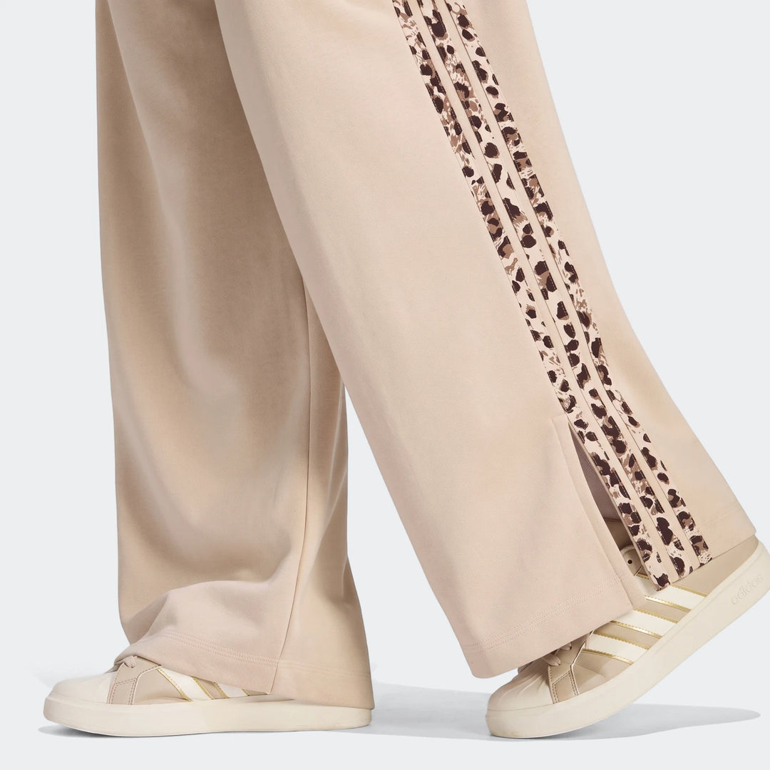 Person's legs wearing beige wide-leg Seasonal Essentials Animal Print 3-Stripes Joggers with leopard print side stripes and