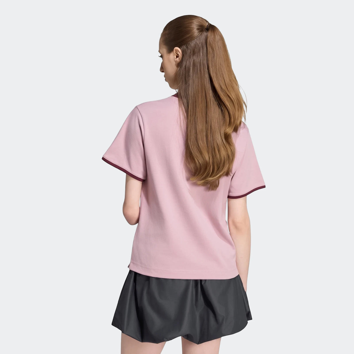 Woman from back wearing a pink Seasonal Essentials Colorpop T-Shirt with dark red trim and a dark gray skirt.