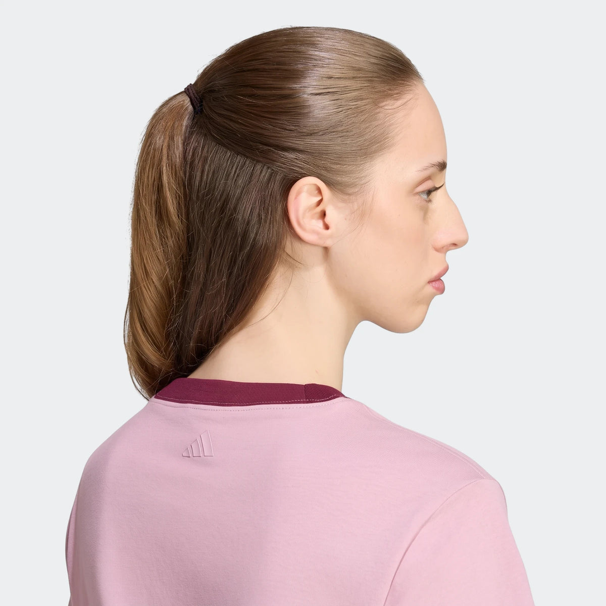 Profile view of a woman wearing a pink Seasonal Essentials Colorpop T-Shirt with a maroon ribbed collar and embossed graphic.