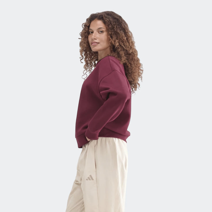 Woman with curly hair wearing a maroon Slim Fleece Crew Sweatshirt and beige pants, hands in pockets, posing for a product