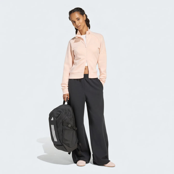 Female model in pink Soft Luxe Slim Track Top, black wide-leg pants, and light pink shoes, holding a black Adidas backpack.