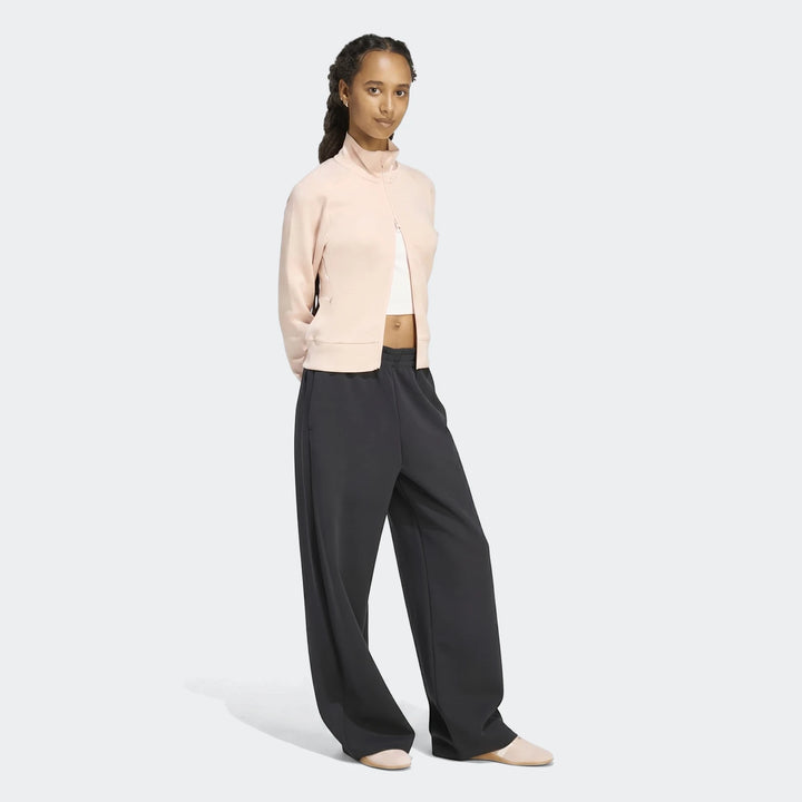 Young woman wearing a pink Soft Luxe Slim Track Top, white crop top, and dark wide-leg pants, full body view.