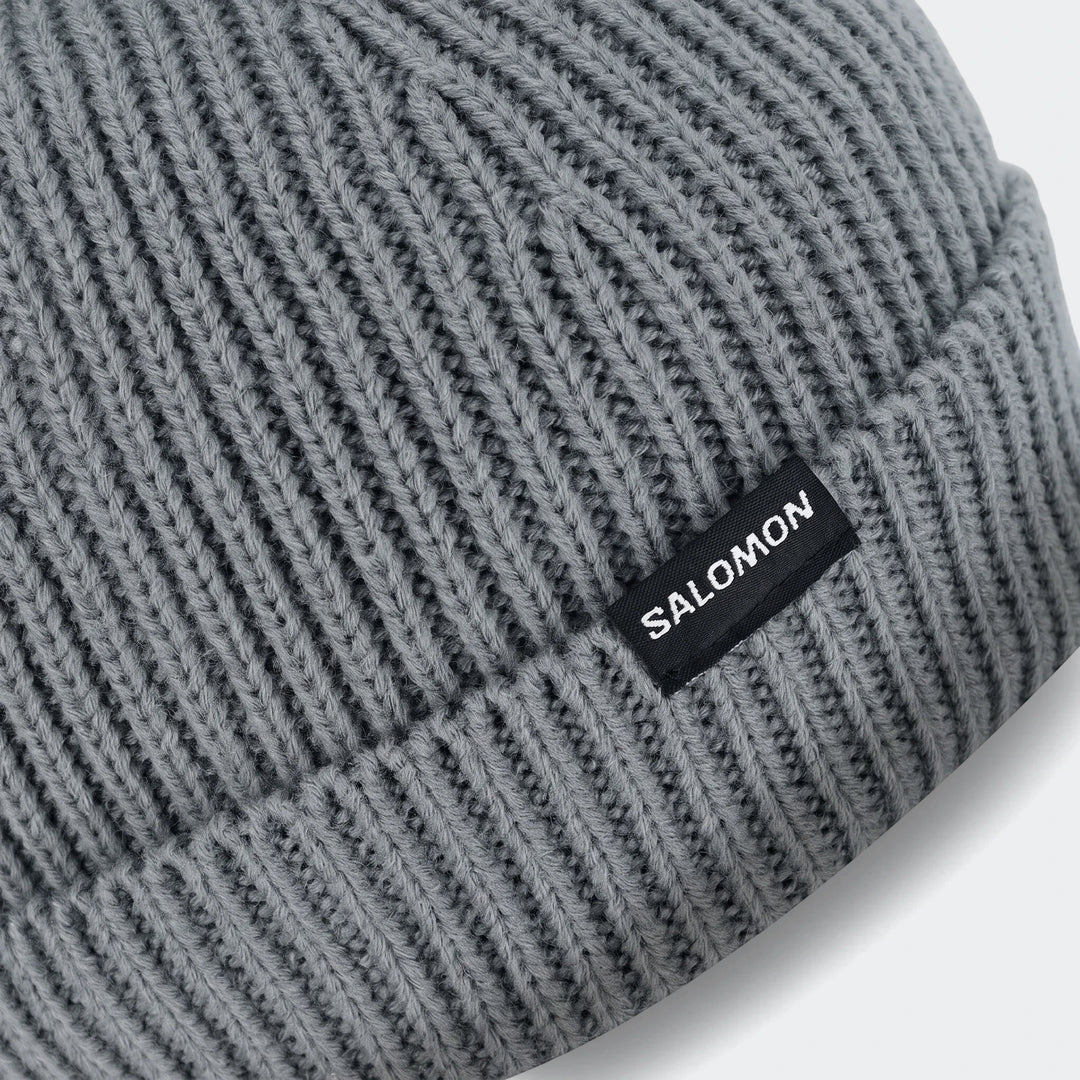 Close-up of a grey Soloman Moss Beanie Ii, featuring a ribbed knit texture and a black woven SALOMON logo label.