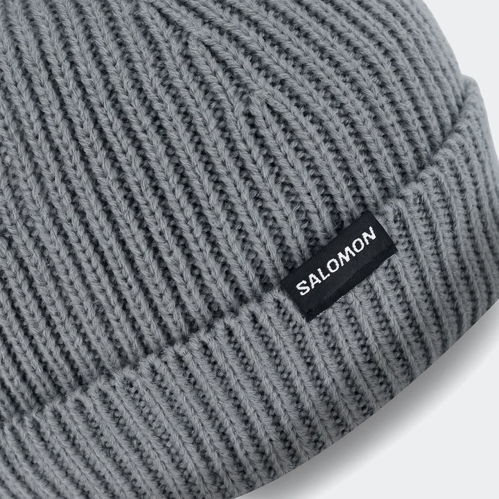 Close-up of a grey Soloman Moss Beanie Ii, featuring a ribbed knit texture and a black woven SALOMON logo label.