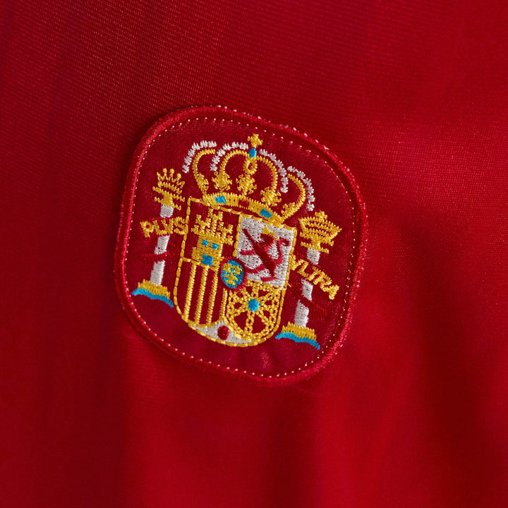 Close-up of the embroidered emblem on a red Spain 1994 Retro Home Jersey, featuring the national coat of arms.