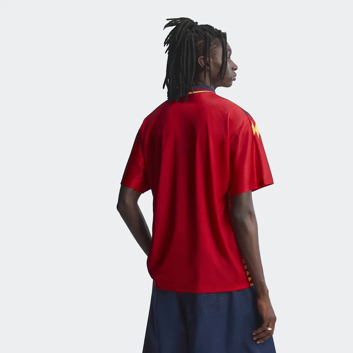 Male model with dreadlocks wearing a red Spain 1994 Retro Home Jersey and dark blue shorts, presented from a back view.