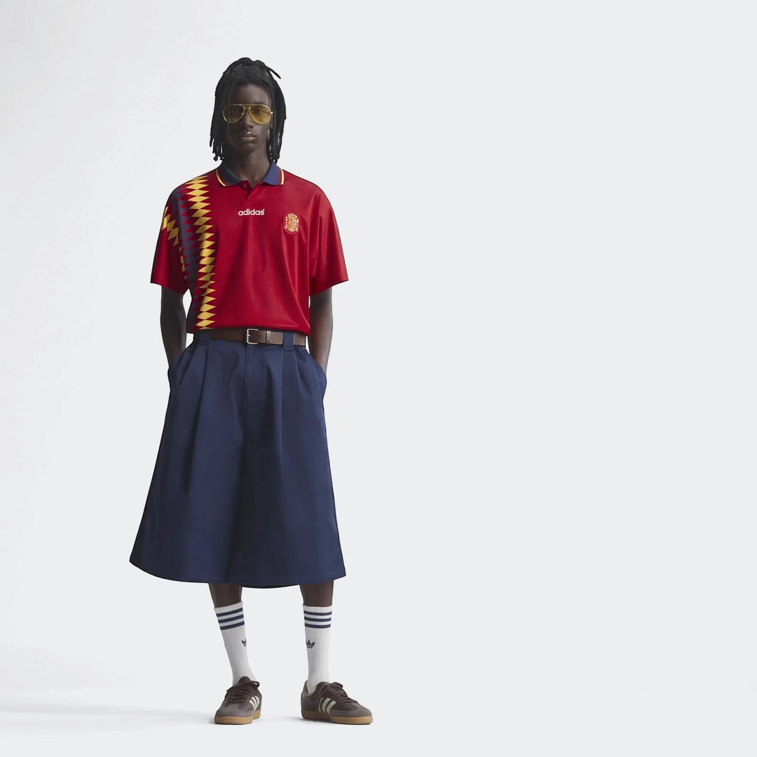Male model wearing a red Adidas Spain 1994 Retro Home Jersey, navy skirt, and brown shoes in a full body shot.
