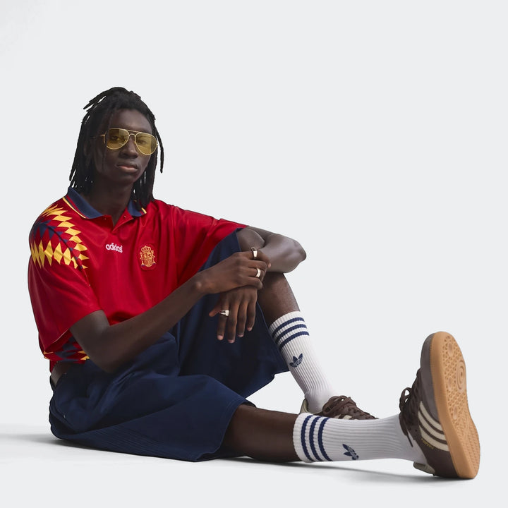 Man wearing an Adidas Spain 1994 Retro Home Jersey, dark blue shorts, white socks, brown Samba shoes, and yellow aviator