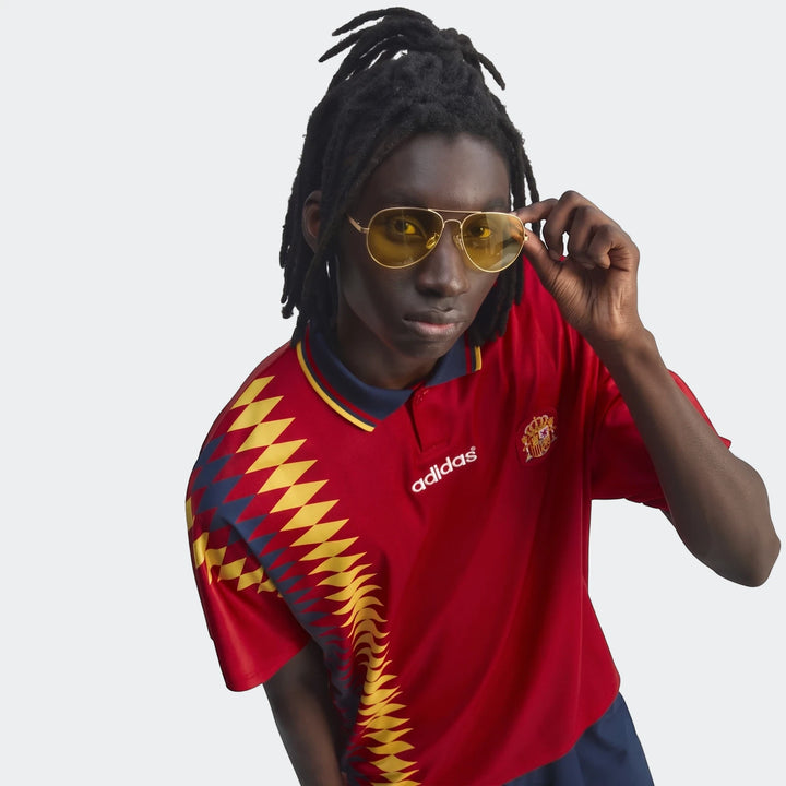 Male model wearing a red Spain 1994 Retro Home Jersey and yellow aviator sunglasses, posing in a studio.