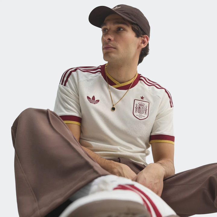 A male model showcasing the white and maroon Spain 25/26 Authentic Away Jersey, featuring the Adidas logo and team crest,