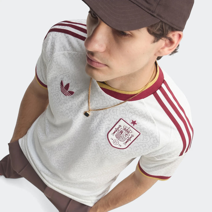 Close-up of a male model wearing the white, maroon, and gold Spain 25/26 Authentic Away Jersey with patterned fabric and