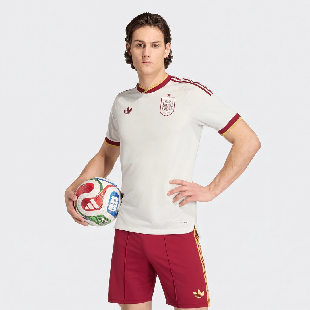 Spain 25/26 Authentic Away Jersey, white with red and gold details, worn by a male model holding a soccer ball.