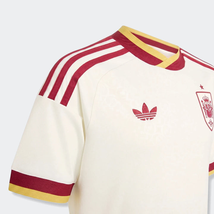Spain 25/26 Away Youth Jersey in cream with red Adidas stripes and national crest, close-up view.
