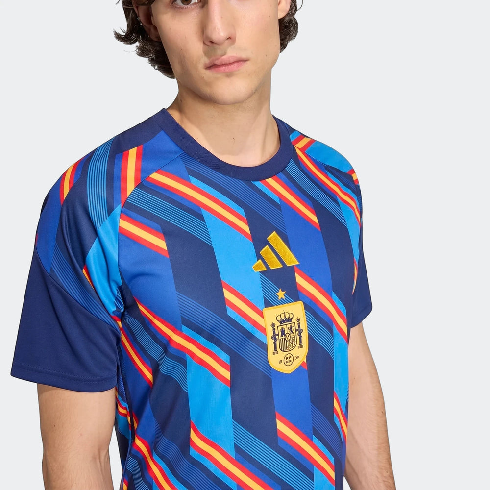 Spain 26 Home Pre Match Jersey in blue, red, and yellow stripes, worn by a man. Features Adidas logo and national team crest.