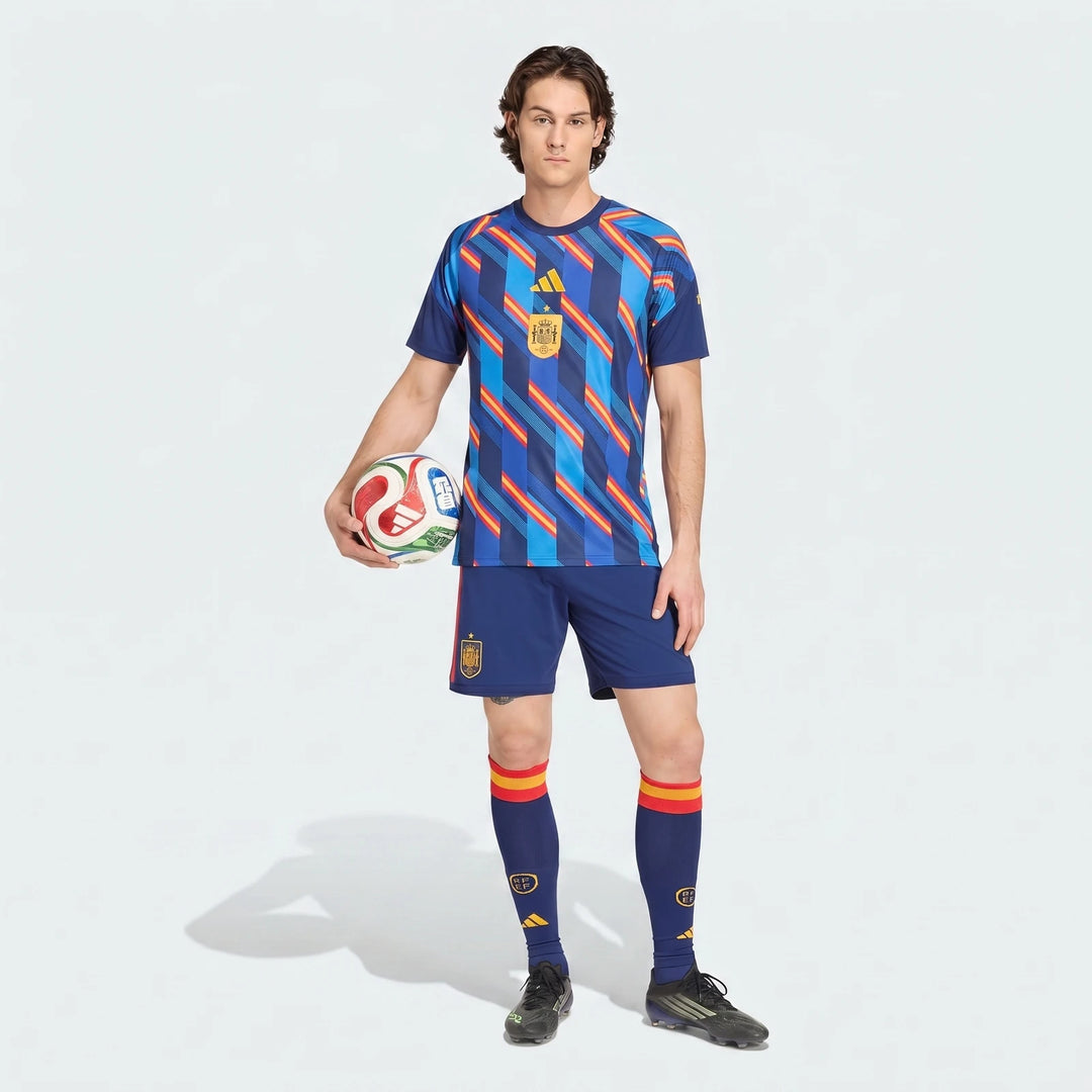 Male model in Spain 26 Home Pre Match Jersey with blue patterned top, blue shorts, and socks, holding a football.