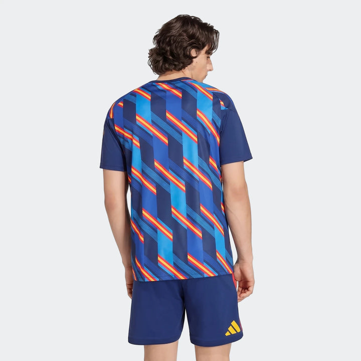 Rear view of a male model wearing the Spain 26 Home Pre Match Jersey and shorts, featuring a blue, red, and yellow geometric
