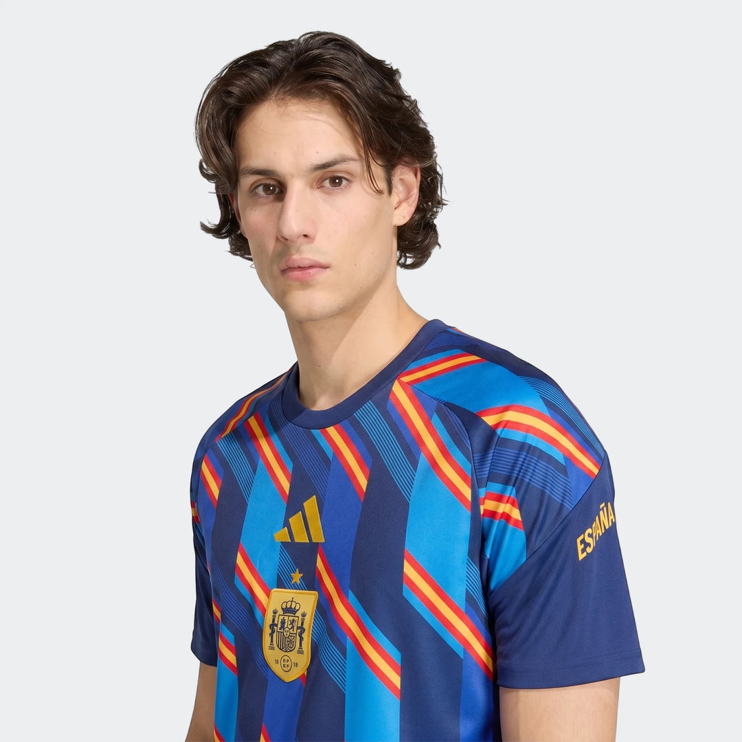 Male model wearing a blue Spain 26 Home Pre Match Jersey with red and yellow striped patterns.
