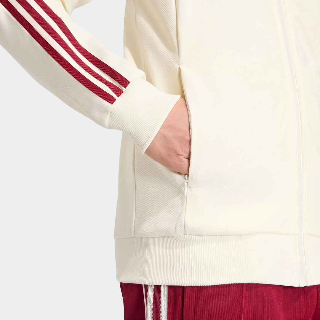 Close-up of an off-white Spain Away Anthem Jacket with red three stripes on the sleeve, featuring a zippered pocket, worn by