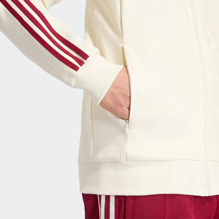 Close-up of an off-white Spain Away Anthem Jacket with red three stripes on the sleeve, featuring a zippered pocket, worn by