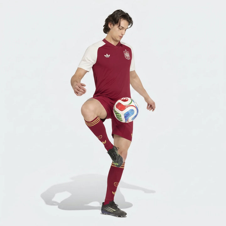 Male model in a maroon and white Adidas Spain Away Pre-Match Shirt, maroon shorts, and socks, juggling a soccer ball.