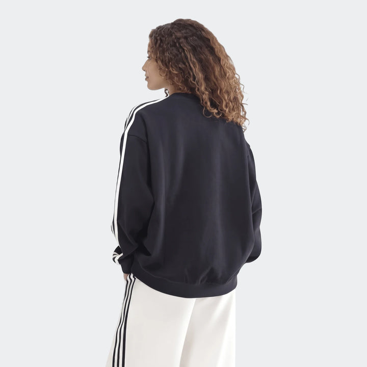 Dark blue Sportswear 3-Stripes oversized crew sweatshirt and white wide-leg pants, back view on a model with curly hair.