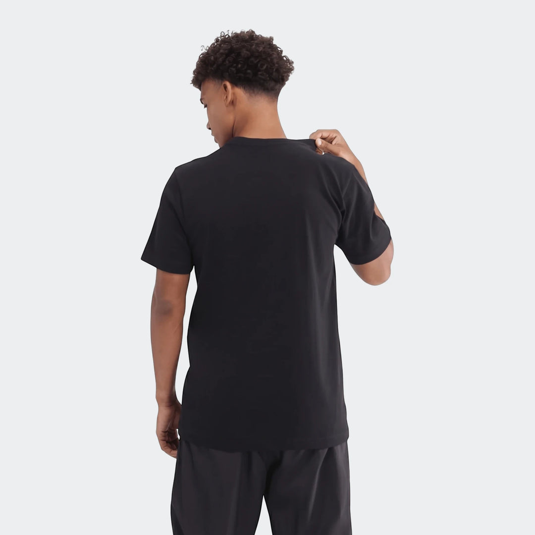 A young man, seen from behind, wears a black Sportswear Badge Of Sport T-Shirt. His right hand gently touches the collar.