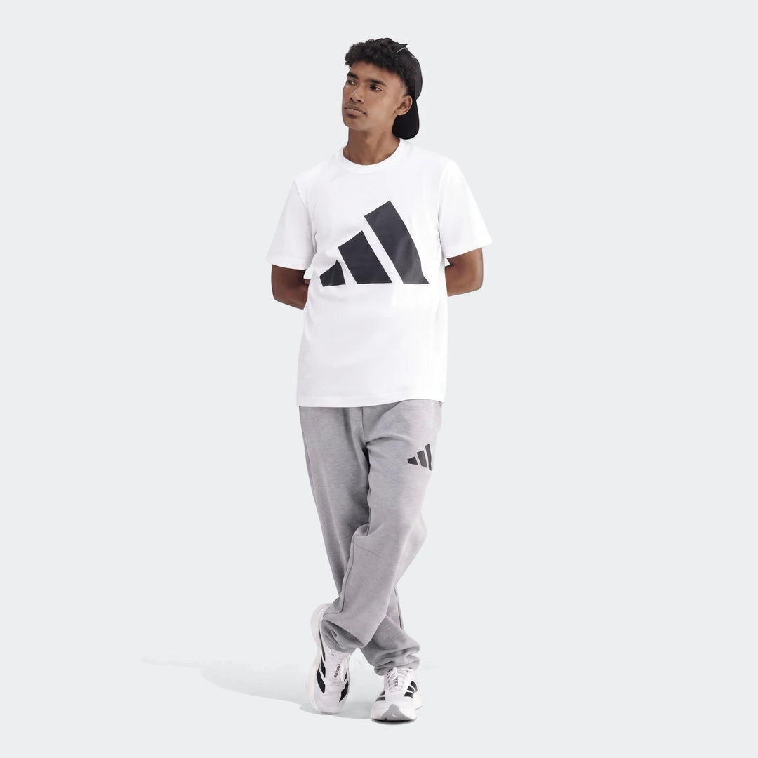 Young man wearing a white Sportswear Badge Of Sport T-Shirt, grey sweatpants, and white sneakers, standing full body.