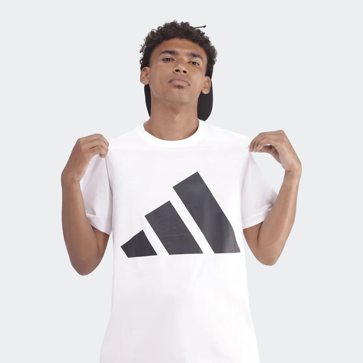 A man wearing a white Sportswear Badge Of Sport T-Shirt with a black logo, shown from the chest up against a gray background.