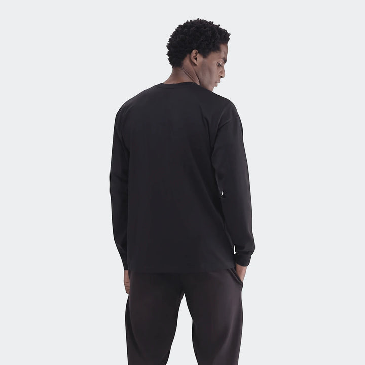 Male model wearing a black Sportswear Open Hem Essentials+ Slim Long Sleeve T-Shirt, photographed from the back, looking