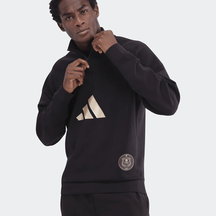 A man models a black Sportswear Open Hem Future Icons 3-Bar Half-Zip Sweatshirt with a gold Adidas logo and an Orlando